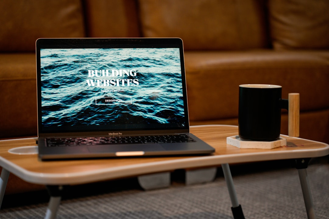 A laptop, MacBook, on top of a portable table with coffee tea mug on the side.